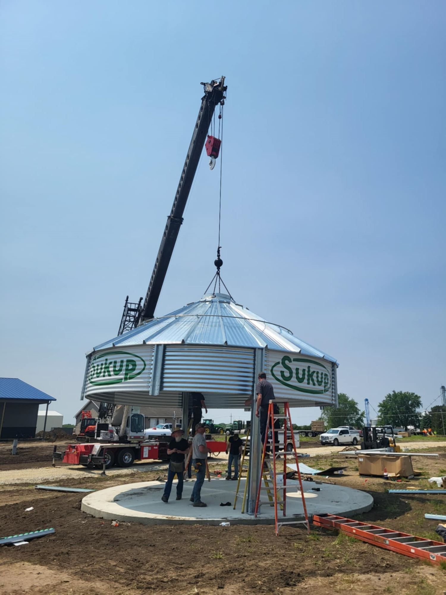 Crane lifting a metal pavilion dome into place at a construction site, with workers below.