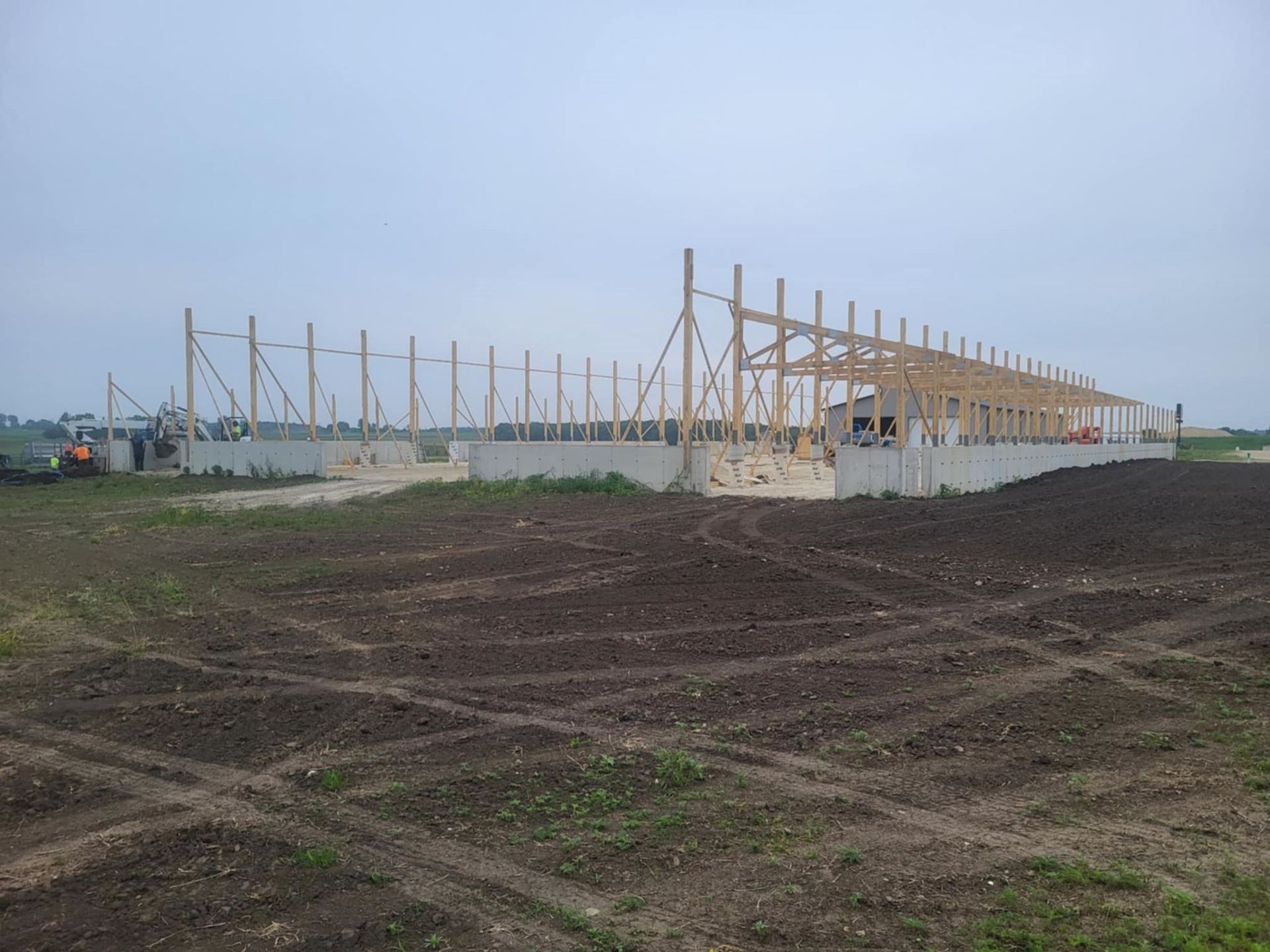Partially built long barn on a dirt field under a cloudy sky