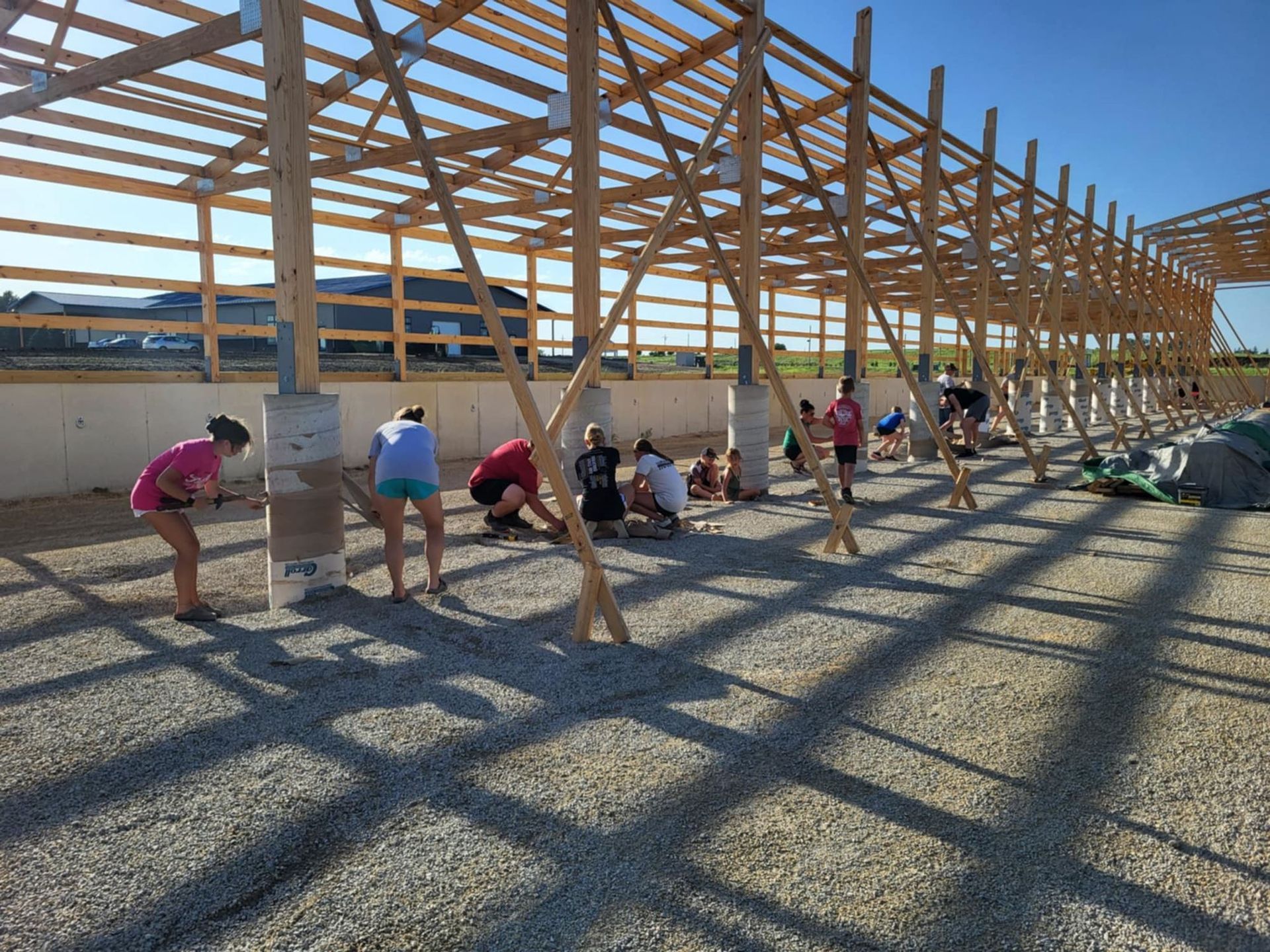 Workers assembling a wooden roof frame on a construction site, with strong grid-like shadows on the ground