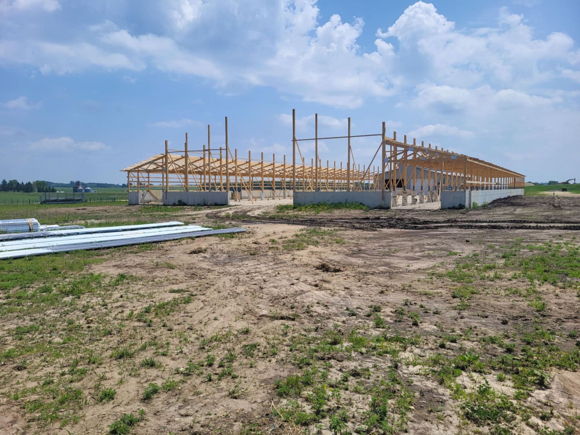 Wooden building frame under construction on a dirt lot beneath a cloudy blue sky