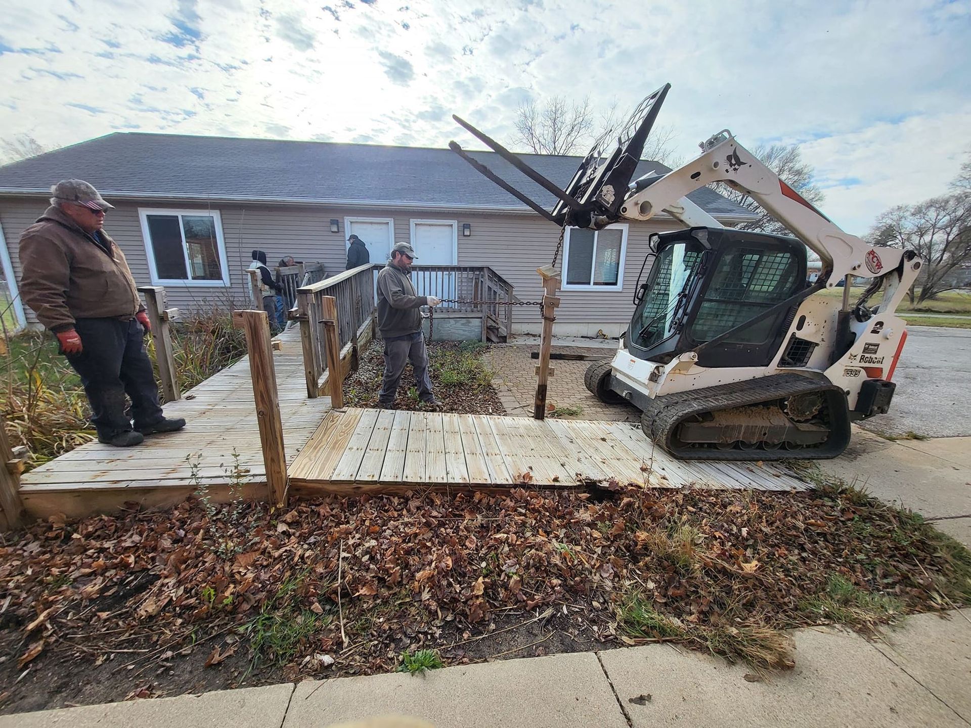 Workers and a skid steer on a wooden ramp beside a house during construction