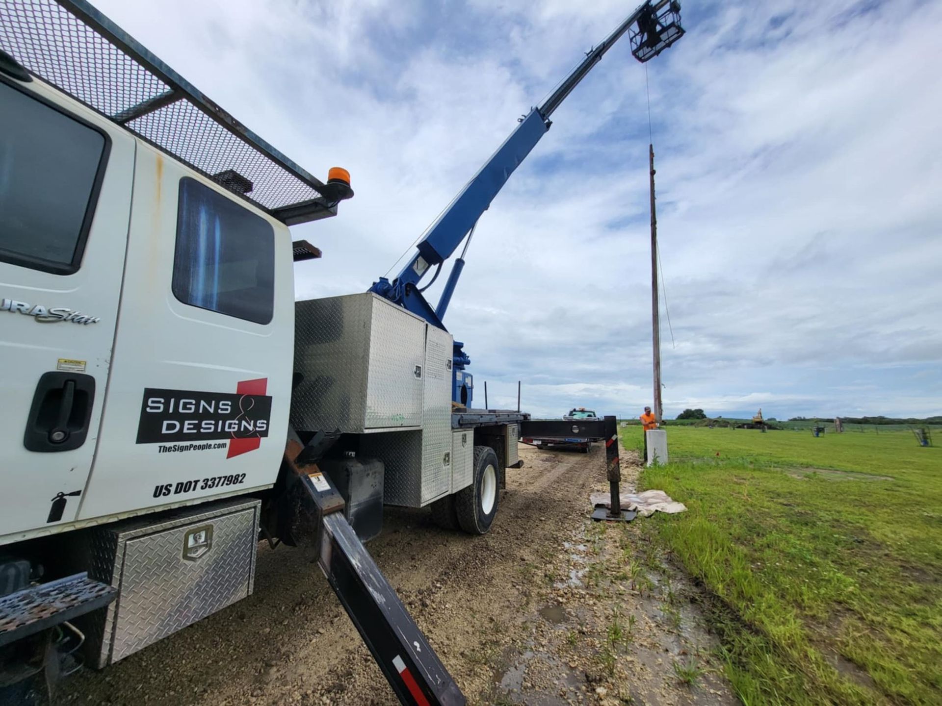 Utility truck with raised boom lift parked on a grassy roadside under a cloudy sky.