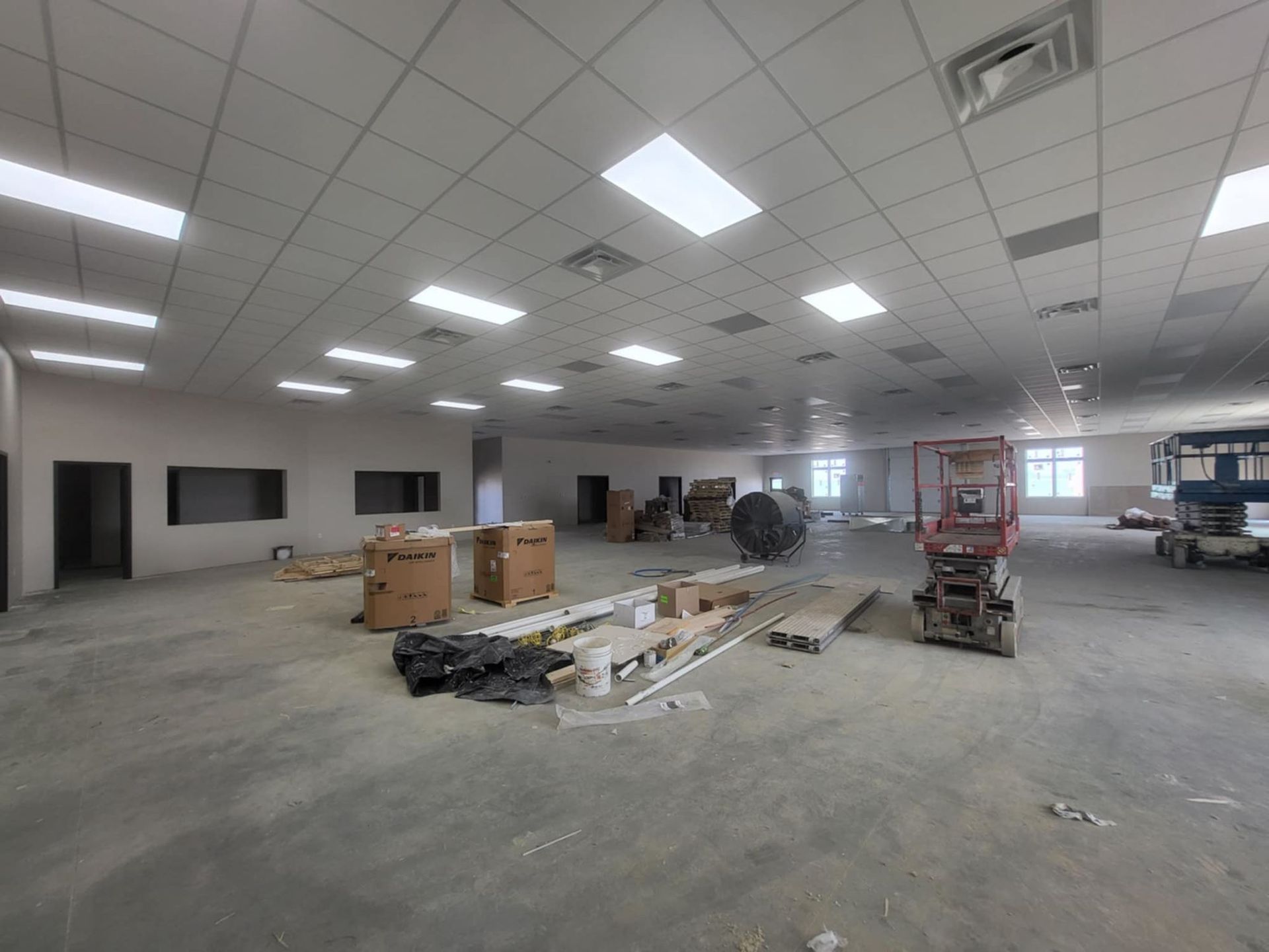 Large unfinished commercial space with concrete floor, ceiling lights, boxes, and construction equipment