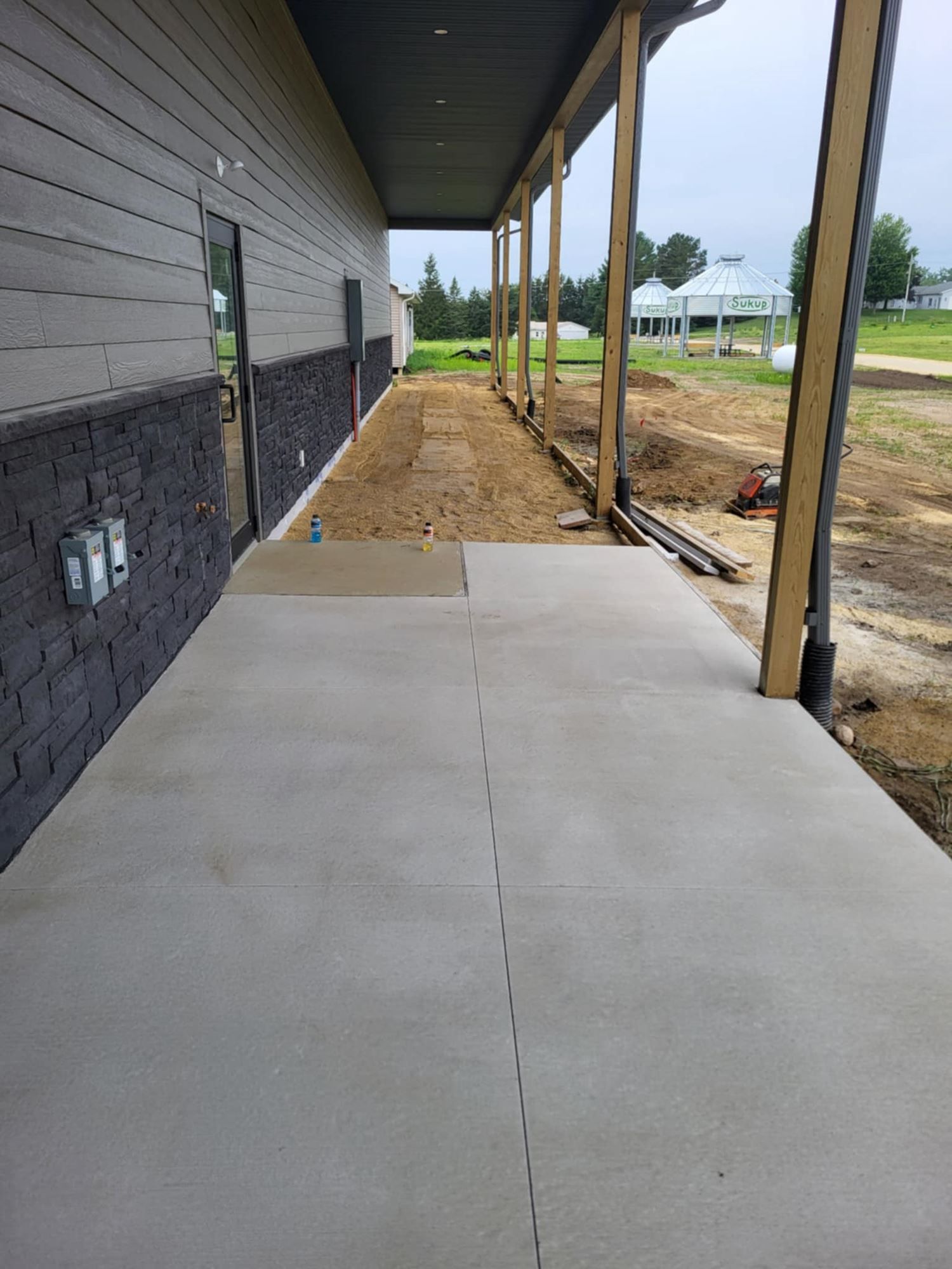 Concrete sidewalk beside a building under construction, with dirt path and support posts along the side