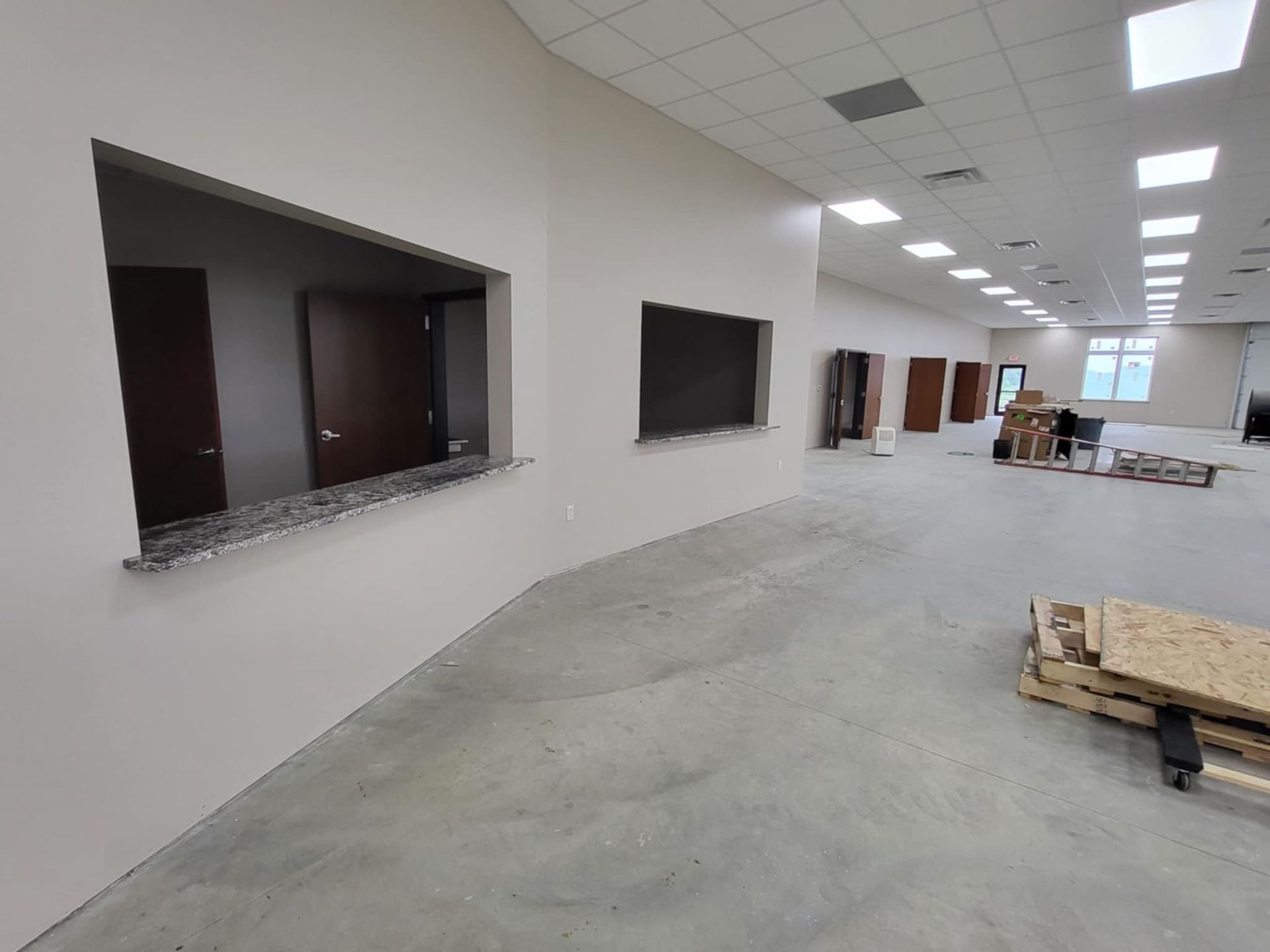 Empty office interior with unfinished walls, window openings, and construction materials on the floor