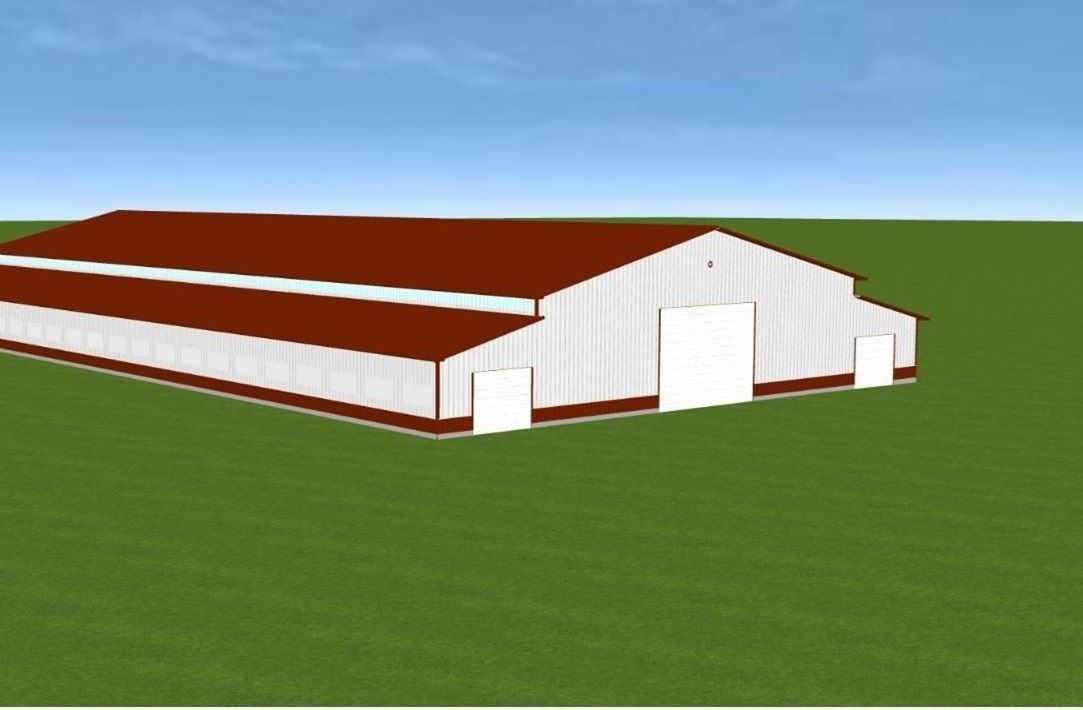 Large white barn with a brown roof on a grassy field under a blue sky