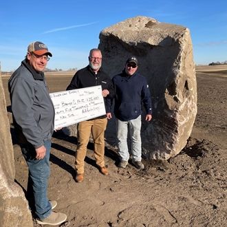 Three people stand beside a large boulder outdoors, one holding a sign.