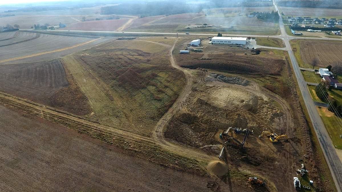 Aerial view of a rural farm field with dirt roads, a small building, and patchy brown grass.