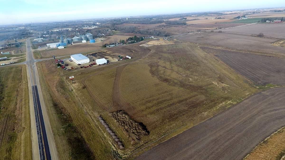 Aerial view of farmland with a road, fields, and a cluster of farm buildings near a pond