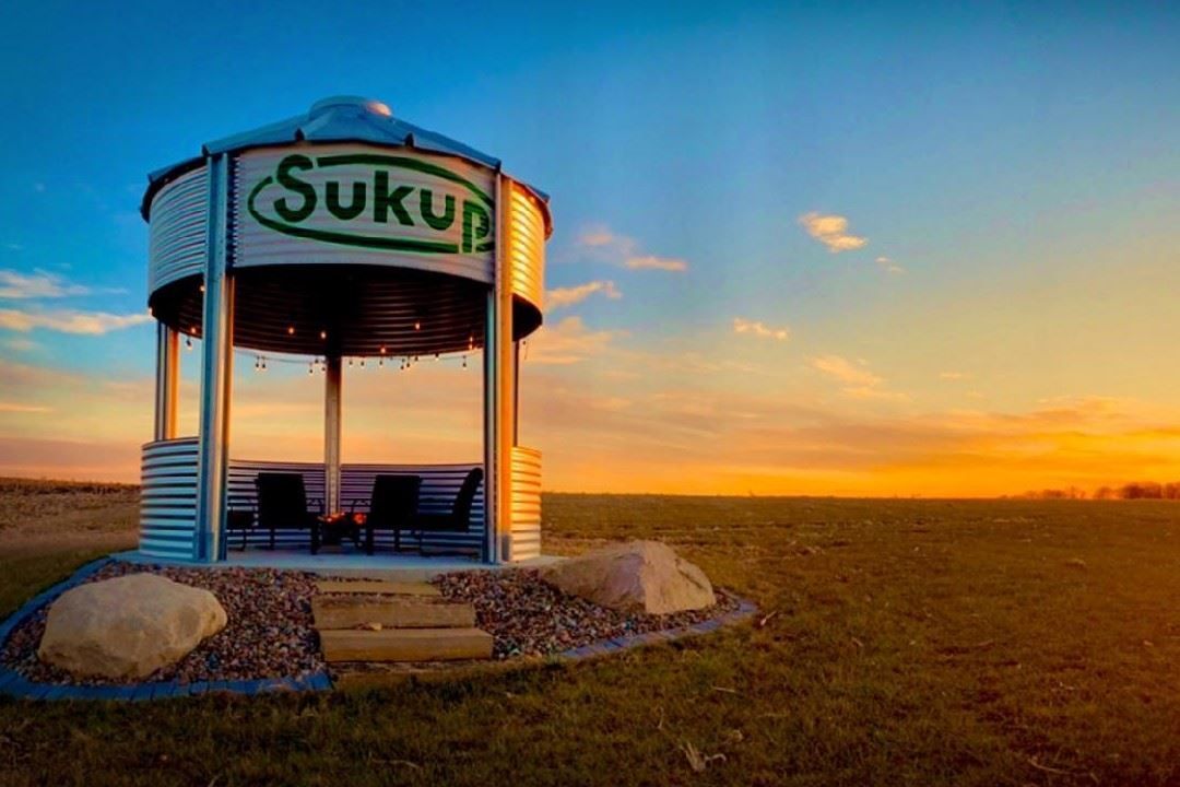 Open-sided shelter with “Suku” sign at sunset over a grassy field