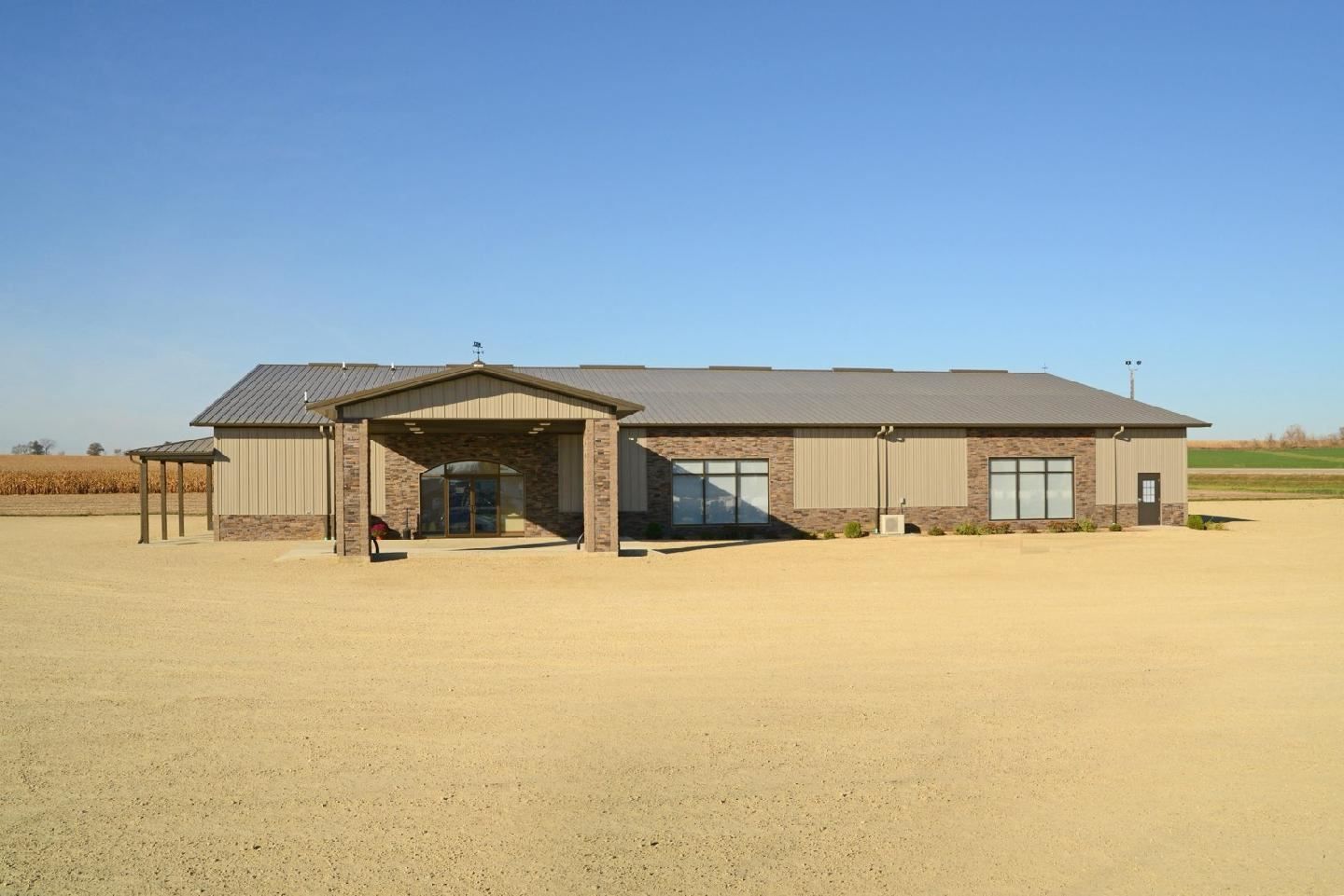 Rural single-story house with a metal roof, carport, and wide sandy yard under a clear blue sky