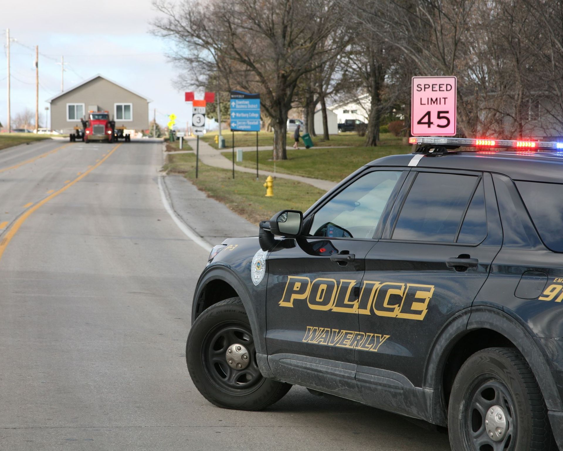 Police SUV with flashing lights blocking a road near a 45 mph speed limit sign and parked building
