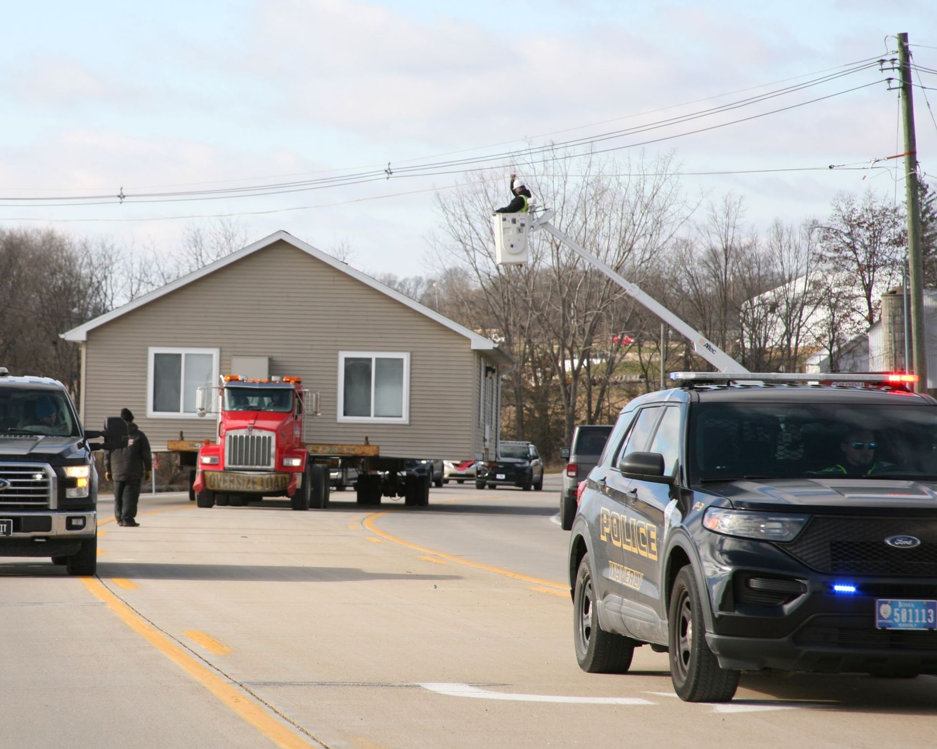 House being transported on a flatbed trailer with police vehicles escorting on a road.