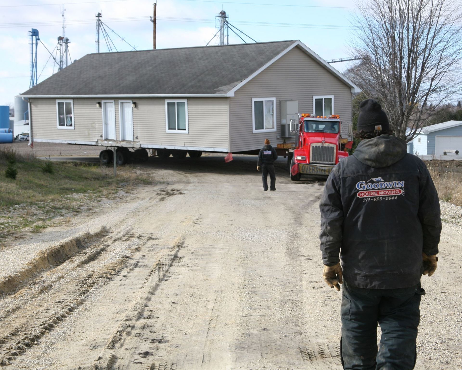 House being moved on a dirt road with workers and a red truck nearby