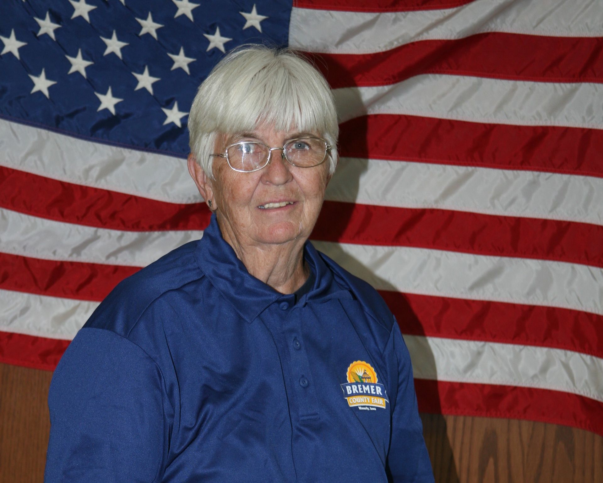 Woman in blue polo standing in front of an American flag and wood-paneled wall