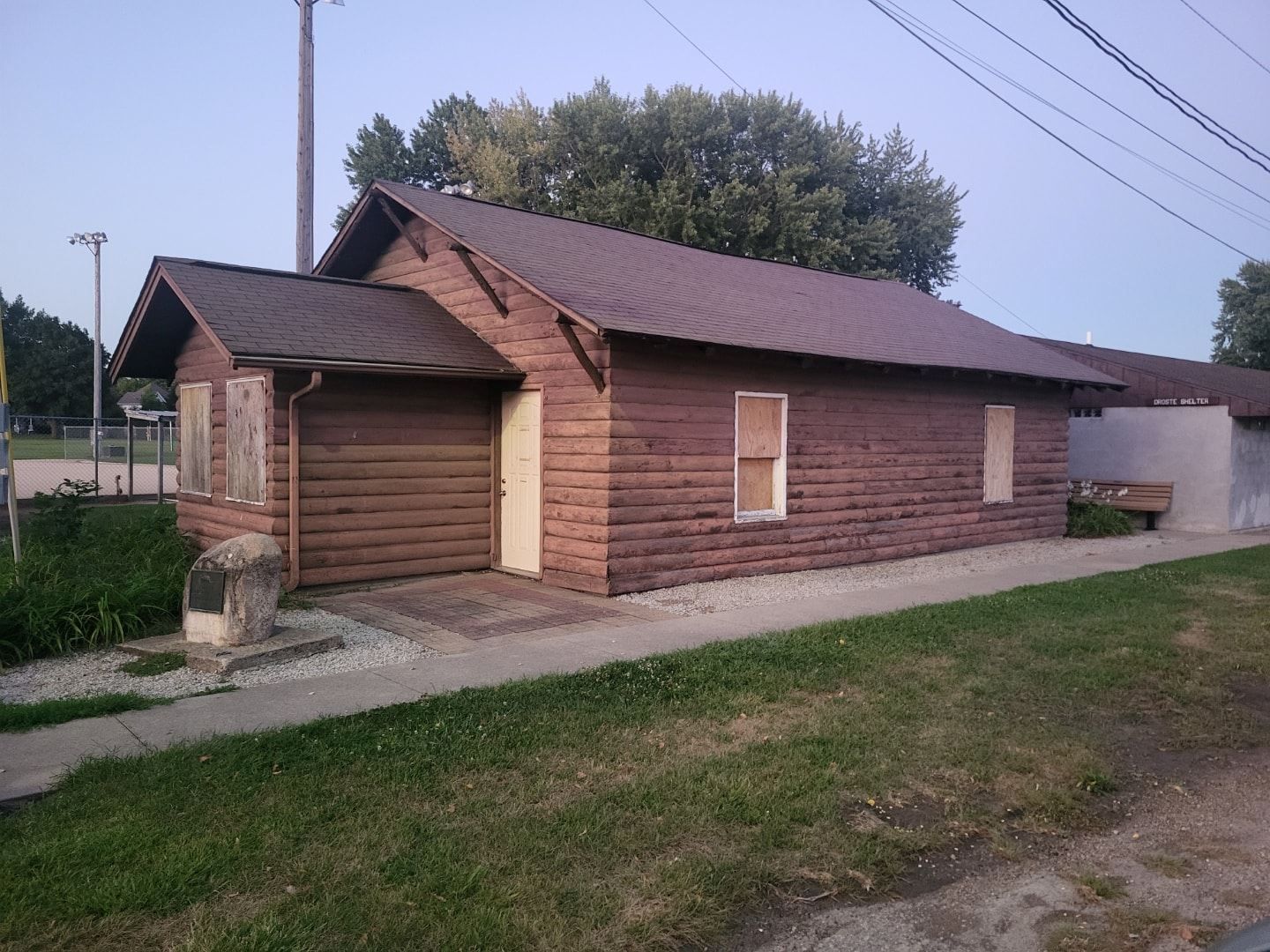 Small brick house with a wooden garage door, seen from a grassy roadside under a clear sky