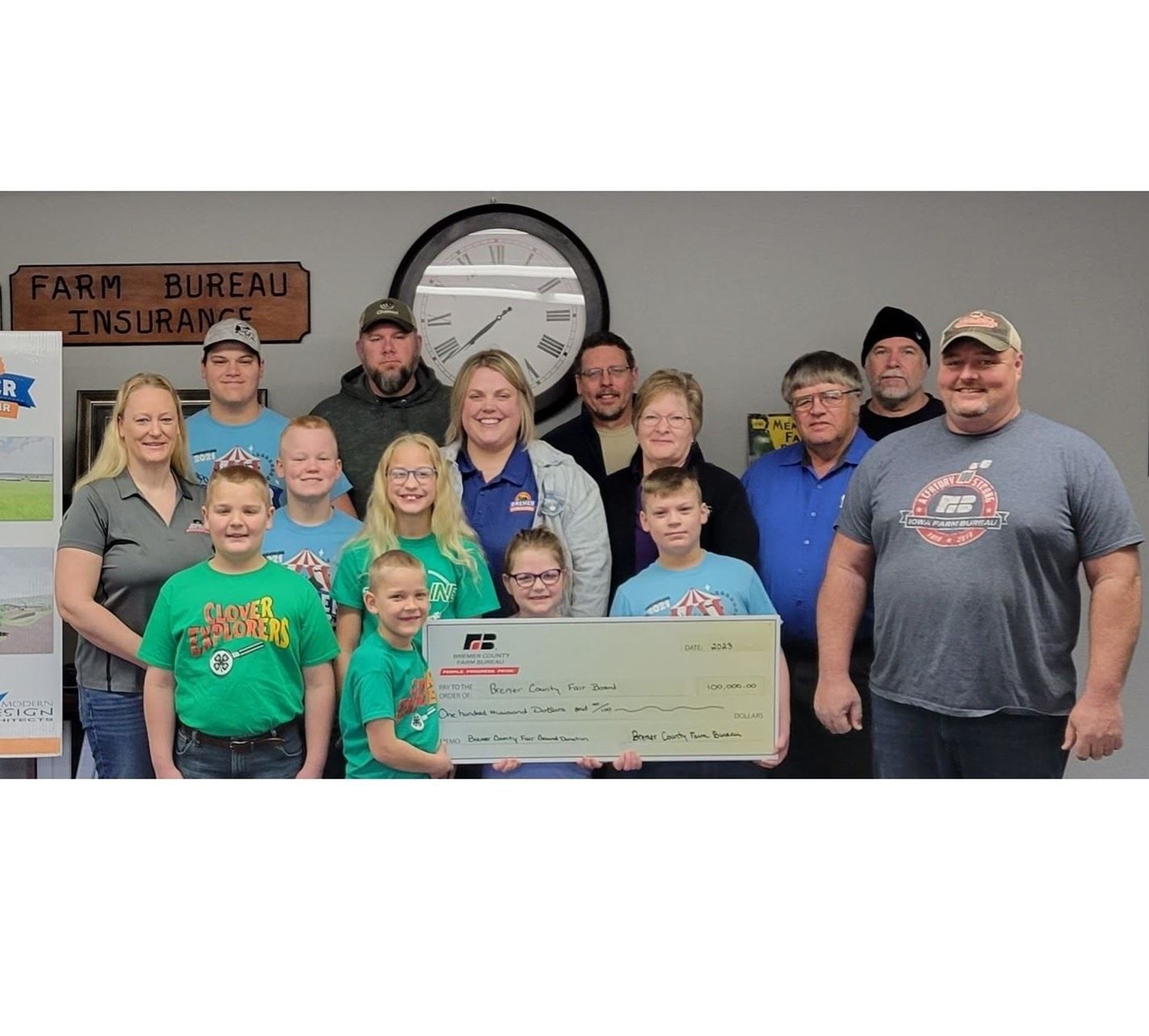 Group posing with a large check in an office, with a Farm Bureau Insurance sign behind them.