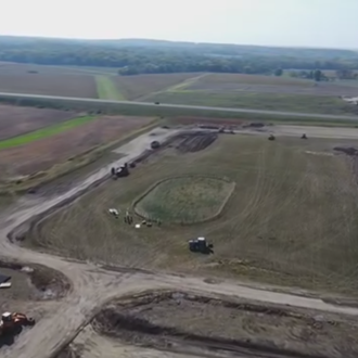 Aerial view of a farm field with dirt roads, earthwork areas, and a few construction vehicles.