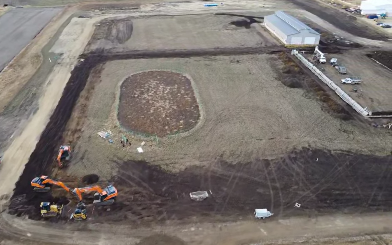 Aerial view of a construction site with excavators, dirt roads, and a large cleared field.
