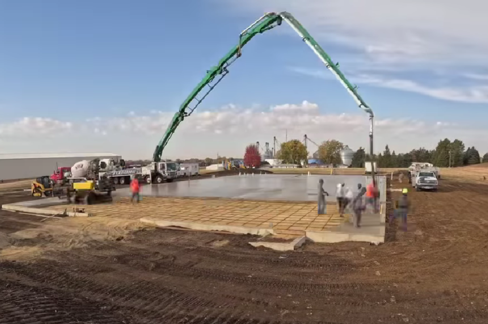 Concrete pump truck pouring a foundation slab at a construction site, workers nearby