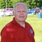 Smiling man in a red polo shirt standing outdoors on a grassy field