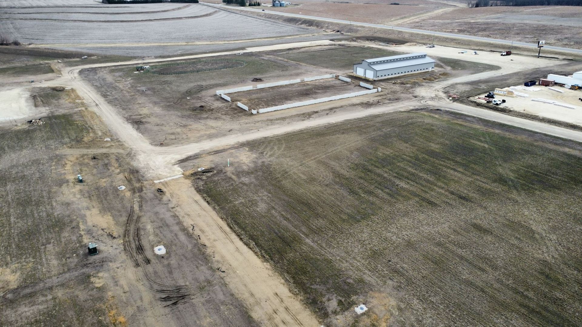 Aerial view of a rural construction site with dirt roads, grassy lots, and a small blue-roofed building.