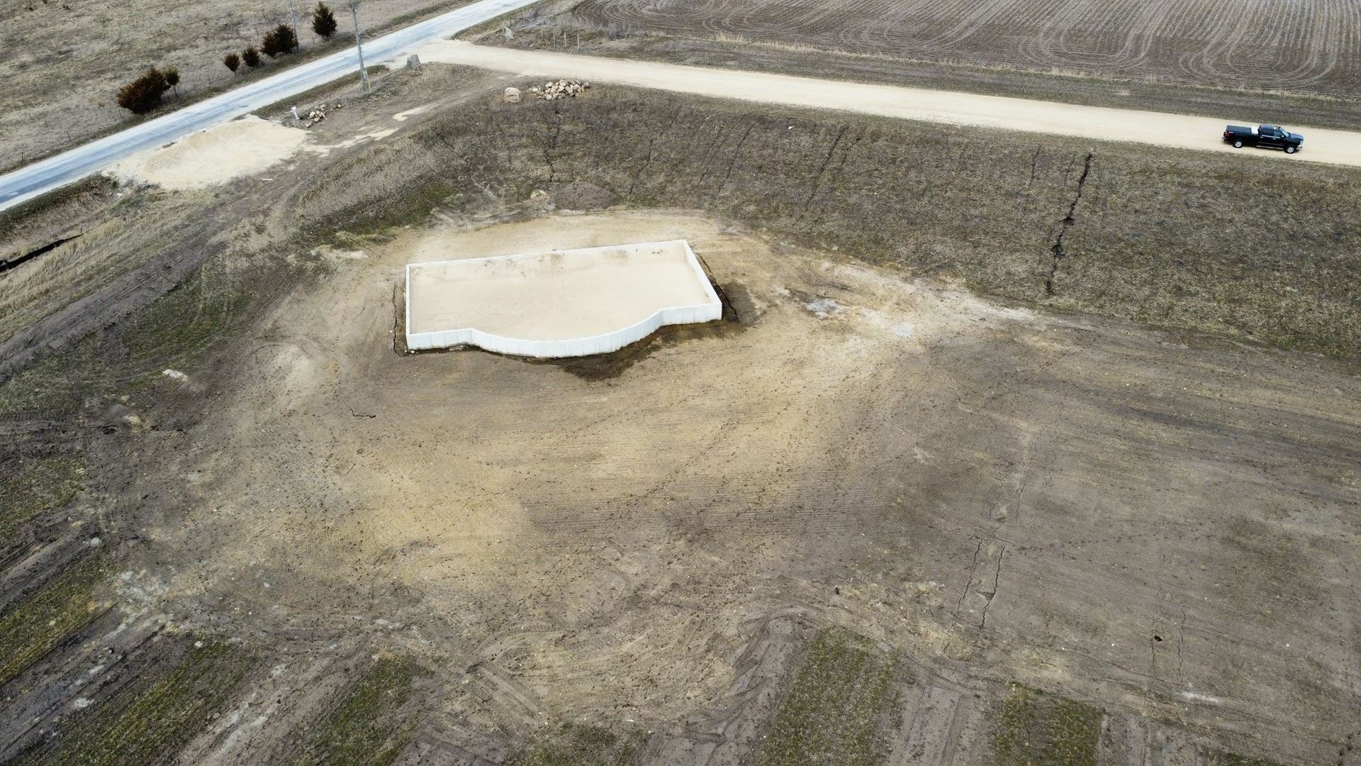 Aerial view of a small concrete slab in a dirt lot beside a road with a parked car