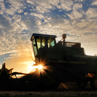 Silhouetted tractor at sunset with sun flare under a cloudy sky