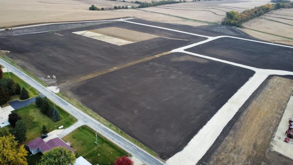 Aerial view of plowed farmland with dark soil plots, pale dirt roads, and a small road along the edge