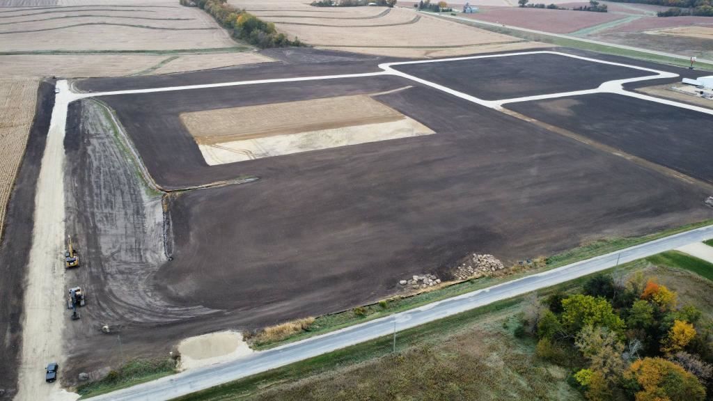 Aerial view of a large dark paved lot with a white rectangular marking and surrounding roads.