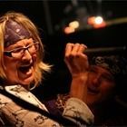 Two people laughing in a dimly lit venue, one holding a microphone on stage