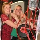 Two people smiling beside a red machine with a large wheel and metal frame
