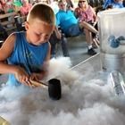 Child pouring from a black cup into a fluffy cotton-like material at a science activity table