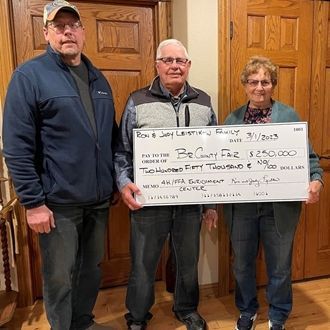 Three people holding a large check in front of wooden doors indoors.