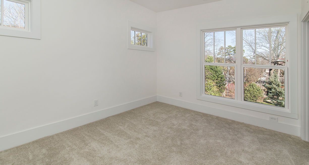 Empty room with beige carpet, white walls, and two windows; one large, one small.
