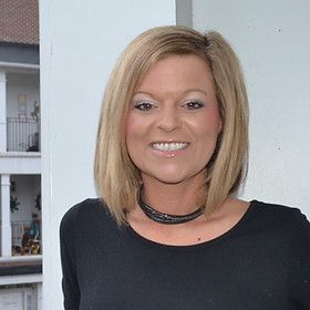Woman with blonde hair wearing a black top smiling outside on a balcony.
