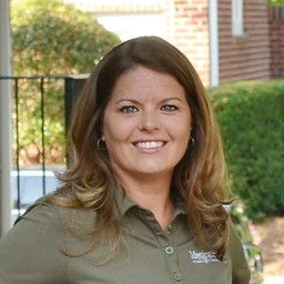 Woman smiling, wearing a green polo shirt outdoors.
