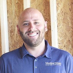 Bald man in a blue polo shirt smiles, wooden wall background,
