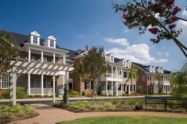 Row of townhouses with white balconies, brick exteriors, and dormers. Landscaped with trees and walkways.