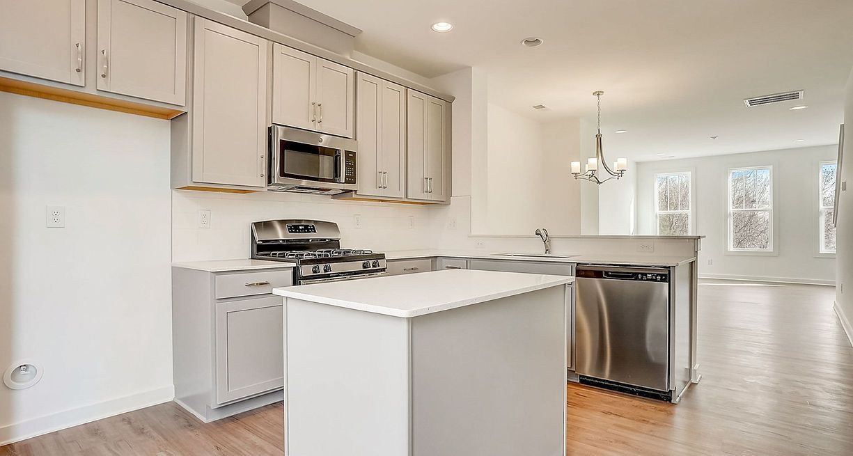 Modern kitchen with gray cabinets, stainless steel appliances, and an island, opens to living area.
