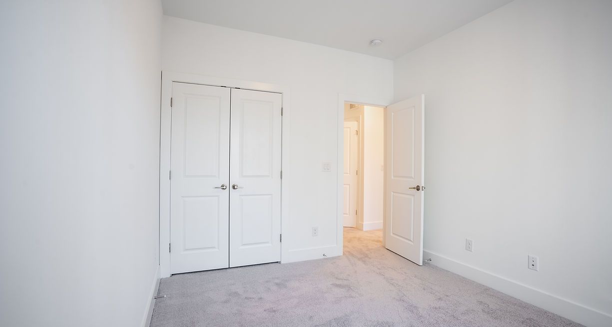 Empty white room with closed closet doors and open doorway.