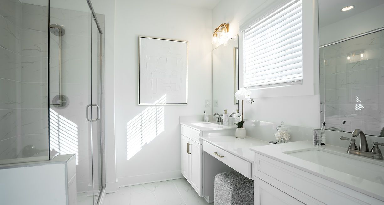 Bright white bathroom with a glass shower, double vanity, and window.