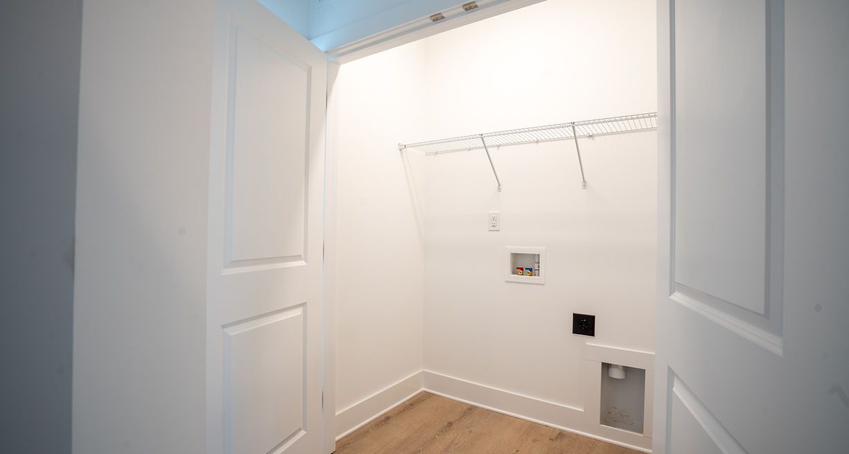 Empty white laundry room with wiring for appliances, shelving, and wooden flooring.