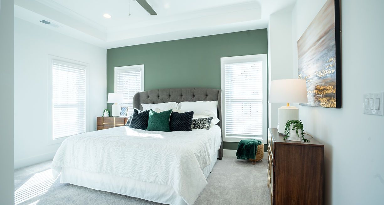 Bedroom with a green accent wall, bed, and two windows with white shutters.
