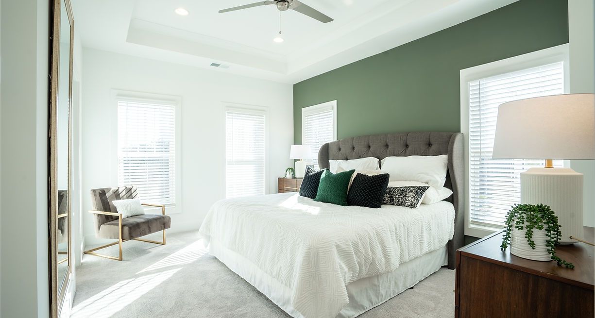 Bedroom with a green accent wall, a bed with white bedding, and a chair in front of a large mirror.