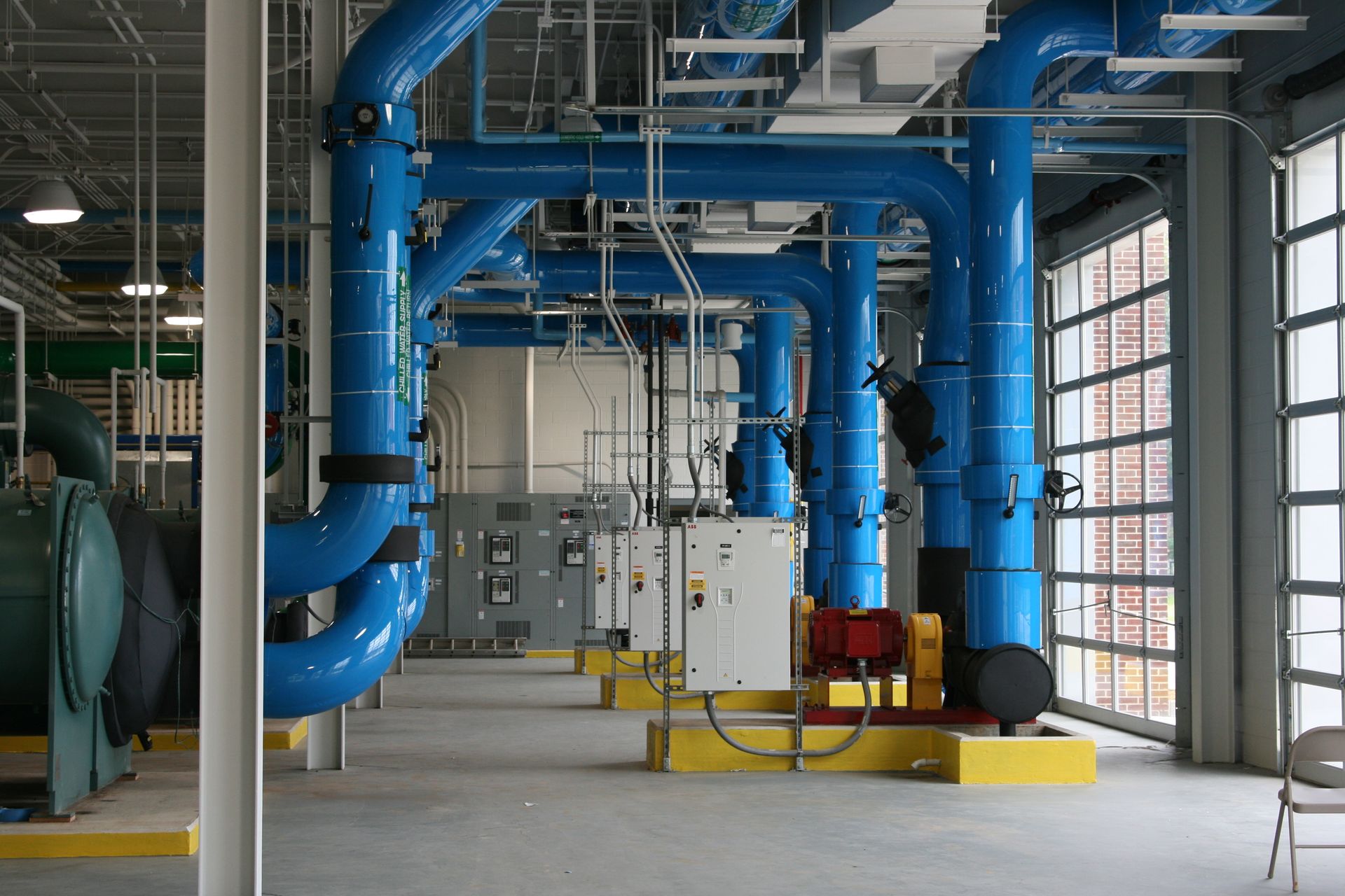 Industrial room with large blue pipes, yellow equipment, and a control panel in a bright utility space