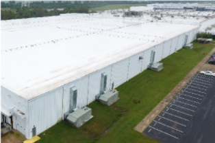Aerial view of a large white warehouse with loading docks beside an empty parking lot.