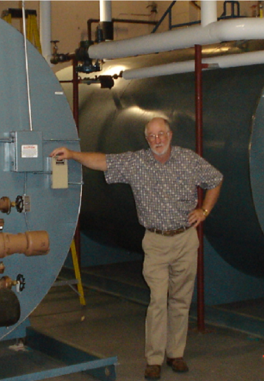 Man standing beside large blue industrial tanks in a basement, leaning on a wall switch.
