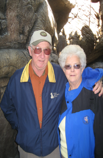 Two people in blue jackets standing close together outdoors by rocks and trees.