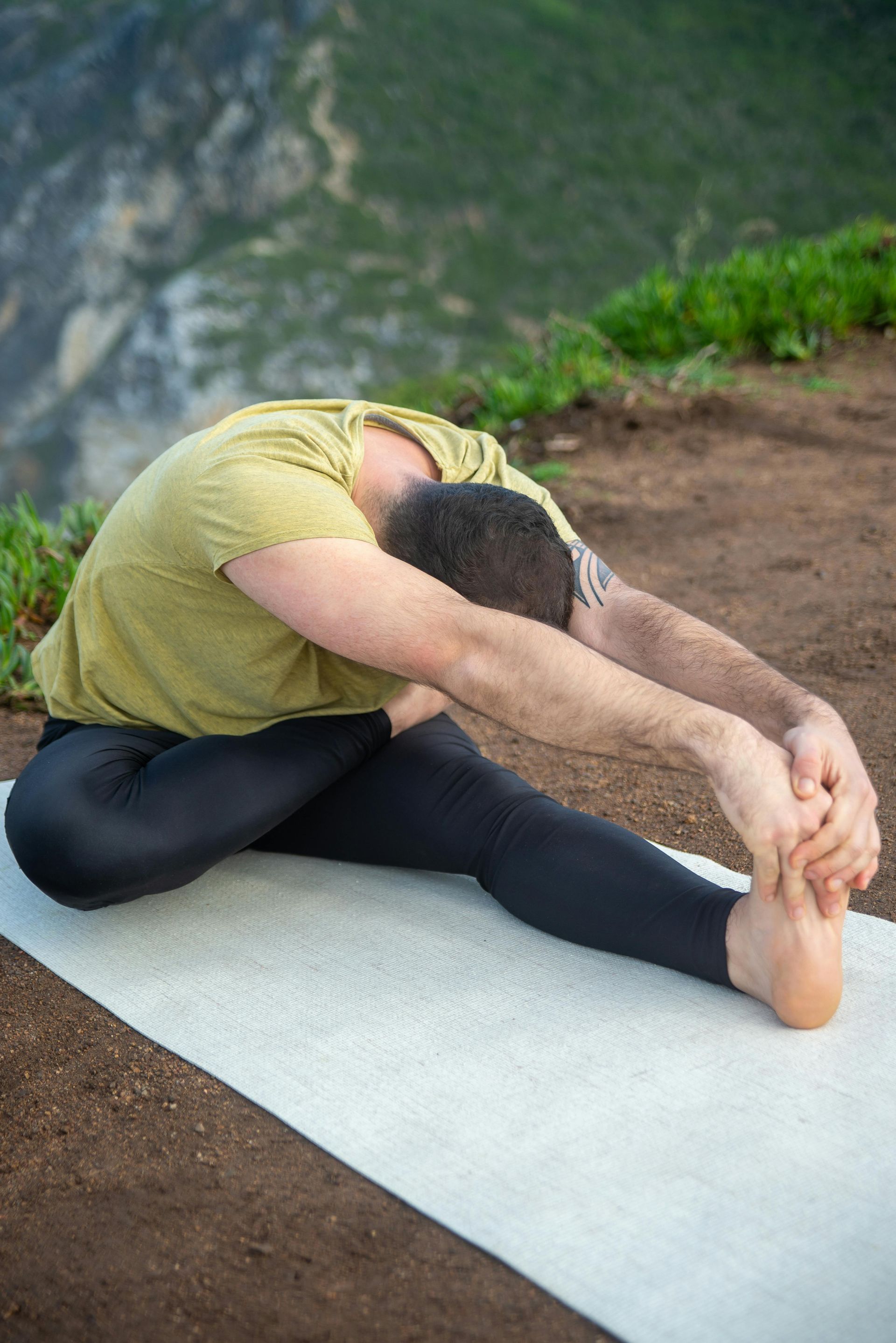 Un homme est assis sur un tapis de yoga et étire ses jambes.